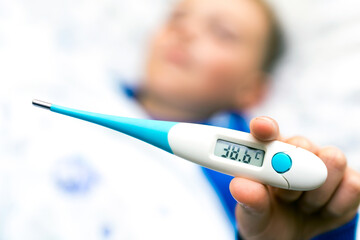 Close up ill young child or schoolboy, lying in bed shows a 38.6 c thermometer, height of his fever