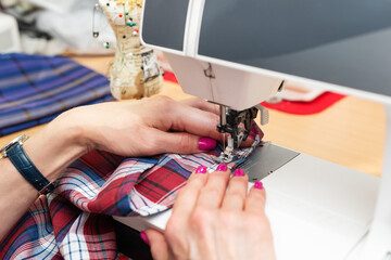 Close-up of women's hands with a beautiful manicure at a sewing machine, with plaid clothes. Concept of sewing, sewing workshop. Side view.