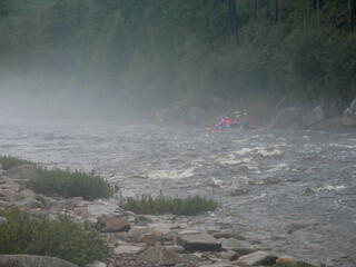 big waves on a mountain river rocks and a swimming vehicle with people on the background of mountains and forests in the fog