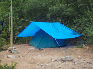 green tourist tent under a blue awning in the forest on a hike