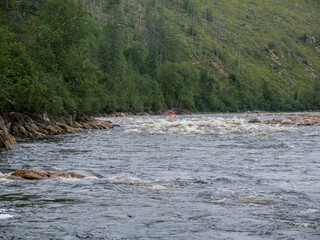 Rifts and rapids on a mountain river against the background of mountains and forests in summer swimming facility in the distance