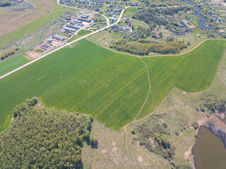 Aerial perspective view of the agricultural landscape.  Roofs of the houses and farms, roads between green grass fields surrounded by forest. Summer day.