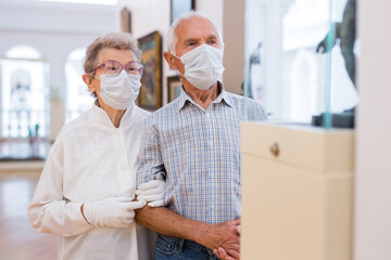 Fototapeta premium mature couple in mask protecting against covid examines paintings on display in hall of art museum