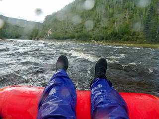 man's feet on the edge of an inflatable boat on the background of a mountain river and mountains
