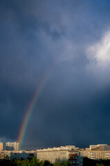 Fragment of the rainbow arc above Moscow city, Russia. Colorful rainbow over roofs of the multi-storey houses and trees after rain and cloudy blue sky as background.