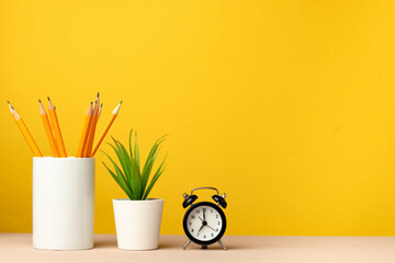 Office cup with pencils and stationery against yellow background