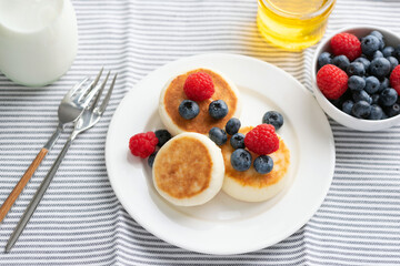 Curd cheese fritters with summer berries and honey served on white porcelain plate. Healthy sweet breakfast food
