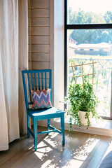 Fototapeta premium Blue chair stands in the room, flower on the window