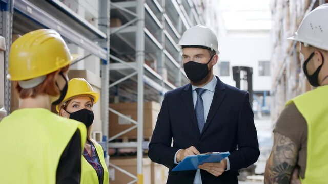 Man manager and workers with face mask standing in warehouse, talking.