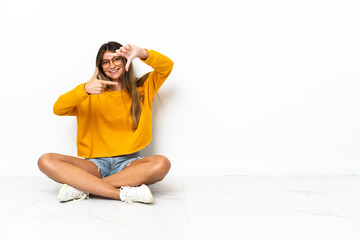 Fototapeta premium Young woman sitting on the floor isolated on white background focusing face. Framing symbol