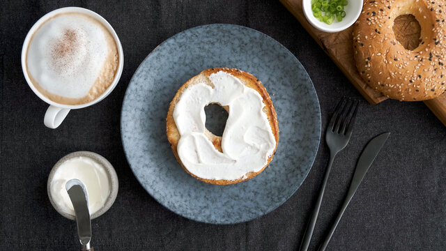 Toasted bagel with cream cheese and cup of coffee for breakfast, top view