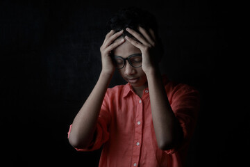 A depressed young boy placing his hands on his head. One light studio shot with shadow