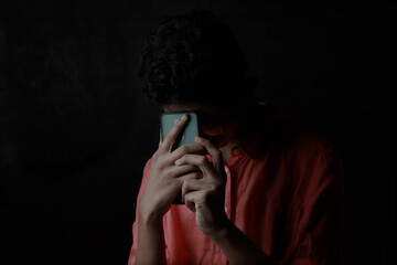 A depressed young boy placing his mobile phone on his forehead in the dark