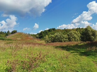 high hills among a green field against a blue sky with clouds on a sunny day