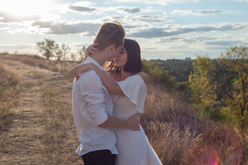 young kissing couple guy with a girl, generation Z. In white. Against the backdrop of a cloudy blue sky, with the rays of the setting sun