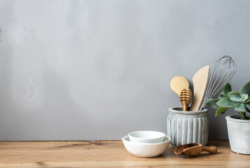 Fototapeta na wymiar Küchenutensilien, weiße Schüsseln und ein Blumentopf auf einem braunen Holztisch. Graue Wand, rustikaler Stil.