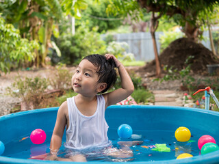 Fototapeta na wymiar Asian cute child boy playing water in blue bowl with relaxing face and wet hair in rural nature. Young kid having happy moment in summer. Family activity at home and preschool concept.