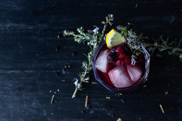 Red Wine Cocktail with berries, rosemary and lemon garnish. Top view with dark wooden background.