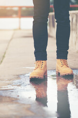 Men wear black jeans and  leather boots walking on puddles on the walkway.