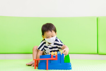 Asian toddler boy playing toy in kids club at hotel.3.5 years old boy child wearing face mask in Day care.Covid-19 coronavirus.Stay home.Social distancing in school.Back to school.New normal behavior.