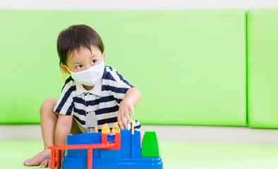 Asian toddler boy playing toy in kids club at hotel.3.5 years old boy child wearing face mask in Day care.Covid-19 coronavirus.Stay home.Social distancing in school.Back to school.New normal behavior.