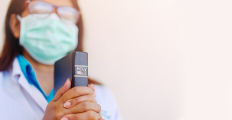 Doctor in uniform holding bible and praying in hospital room with hope.Coronavirus Covid-19.Church online in sunday service. Doctor with faith and praying to GOD.Religion during covid-19 crisis.