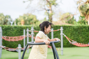 Naklejka premium Asian kid girl playing on a swing and having fun in park.Little asian girl climbing rope at playground.Asian child girl playing on playground in outdoor park.Happy Little asian girl outdoor play park.