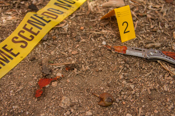 close-up of a crime scene with yellow numbered cards the police tape with the words do not pass and the weapons such as knife and gun used for the crime