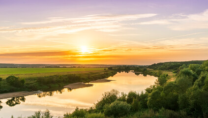 Scenic view at beautiful summer river sunset with reflection on water with green bushes, grass, golden sun rays, calm water ,deep blue cloudy sky and glow on a background, spring evening landscape