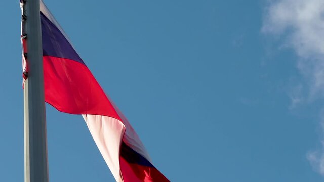 Russian flag fluttering in the wind. National flag against a blue sky, high flagpole
