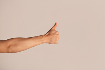 Unrecognizable millennial guy showing thumb up gesture over light background, closeup