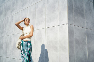 Attractive female model smiling and posing over gray concrete wall in the street, urban style, copy...