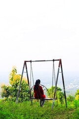 Woman swinging on swings over the green mountain landscape with sky. Freedom concept. Touristic place.