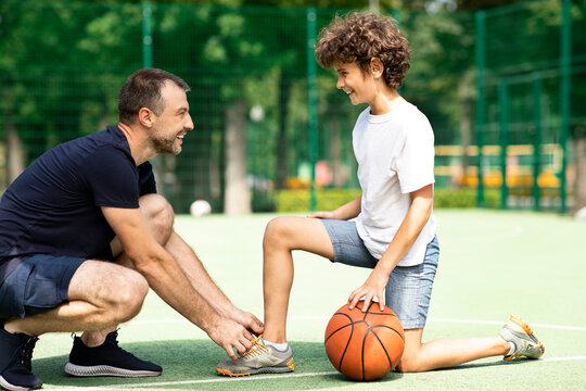 Smiling man tying shoelaces of curly boy on field