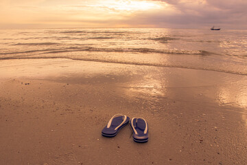 Fototapeta na wymiar Beautiful waves on the beach and blue sandals with in sunrise. 