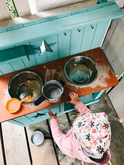 Einjähriges Mädchen spielt draußen an ihrer Matschküche