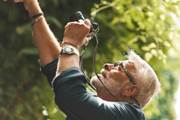 An inquisitive elderly man photographs plants in the forest. Retired tourist is exploring nature.