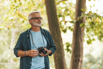 An active hobby of an elderly man with a beard outdoors. A pensioner takes pictures of nature with a camera while traveling.