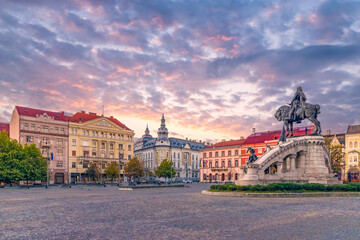 Cluj-Napoca city center. View from the Unirii Square to the Rhedey Palace, Matthias Corvinus Monument and New York Hotel at sunset on a beautiful day - obrazy, fototapety, plakaty