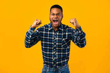 Naklejka premium Emotional African Man Shouting Loudly Shaking Fists Over Yellow Background