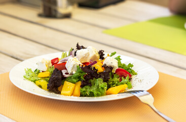 Greek salad on a white plate in a summer cafe. Vegetarian dish. Olives, purple onions and feta cheese. Light snack in a cafe. Summer menu. Natural light.