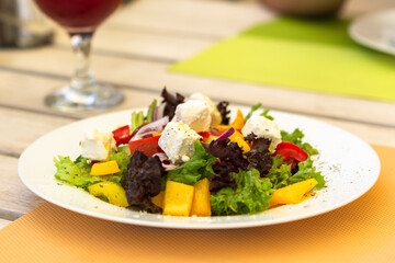 Greek salad on a white plate in a summer cafe. Vegetarian dish. Olives, purple onions and feta cheese. Light snack in a cafe. Summer menu. Natural light.