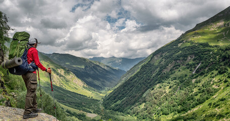 Active man with backpack and camping equipment at Imereteinka river valley background in Karachay-Cherkess, Russia