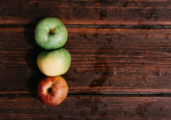 Fresh apples, autumn harvest. Three apples - green, yellow, and red-lie on a wooden table. Fresh apples on a wood textured brown background, mahogany material.