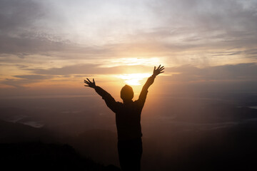 Fototapeta premium Silhouette women standing on cliff and see sun up.She is raise hand up and enjoying fresh air.She enjoying free happiness in beautiful Thailand landscape. photo concept active and nature background.