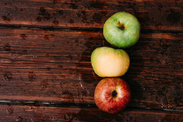 Fresh apples, autumn harvest. Three apples - green, yellow, and red-lie on a wooden table. Fresh apples on a wood textured brown background, mahogany material.