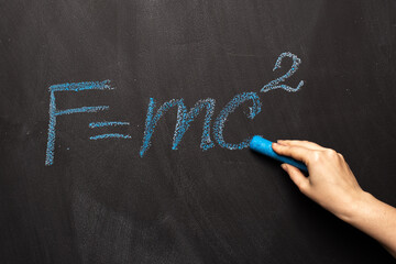 The physical formula of Einstein's theory is written in blue chalk on a blackboard. FMC2 is written...