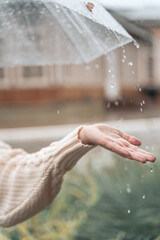 Woman hand caching rain drops from umbrella in the rain