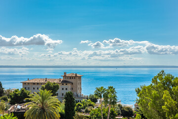 Naklejka premium Building in front of the sea with trees in the foreground, in the background views of the sea and the blue sky with white clouds