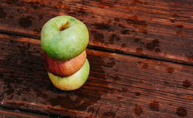 Pyramid of three apples. Fresh apples, autumn harvest. Three apples - green, yellow, and red-lie on a wooden table. Fresh apples on a wood textured brown background, mahogany material.